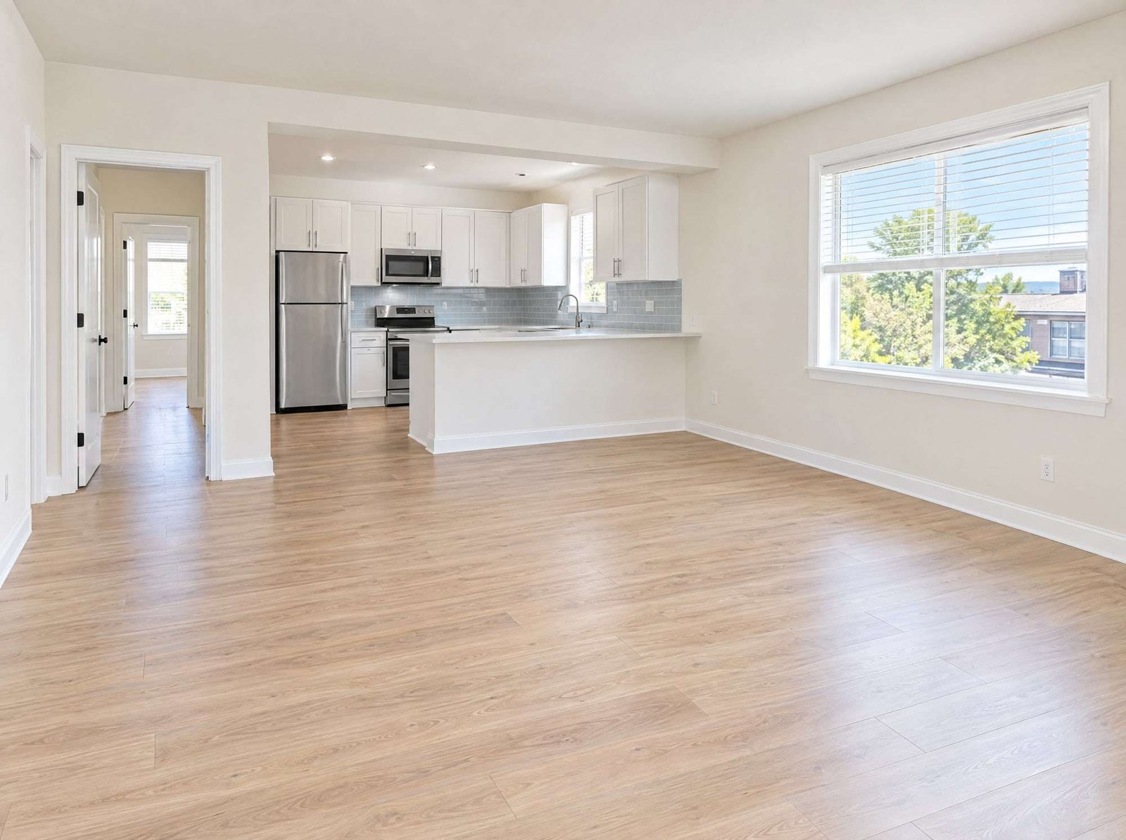 An empty, freshly painted apartment with light wood-look floors, white trim, and a white kitchen in the background.